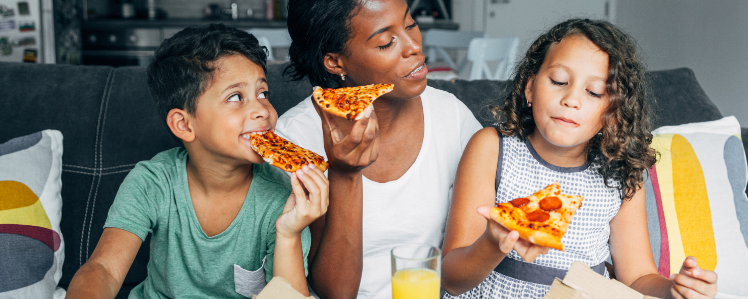 african american mother and two children eating pizza on couch 