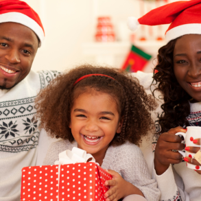 family of three sitting on couch with mugs and santa hats, christmas tree in background