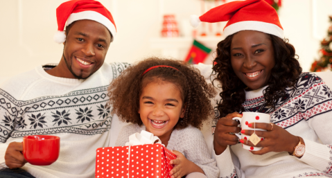 family of three sitting on couch with mugs and santa hats, christmas tree in background