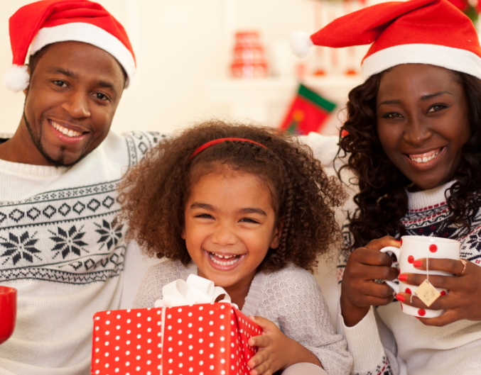 family of three sitting on couch with mugs and santa hats, christmas tree in background
