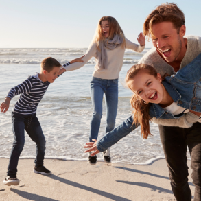 family of four in warm clothes playing on beach