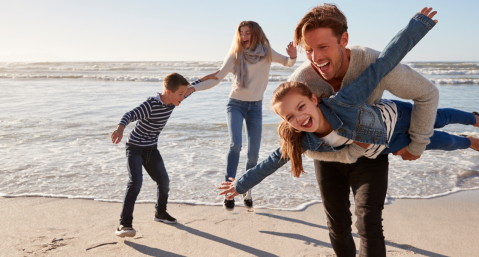 family of four in warm clothes playing on beach